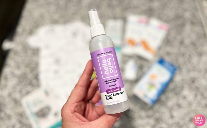 Hand Holding a Hello Bello Hand Sanitizer Spray in Front of a Table Top