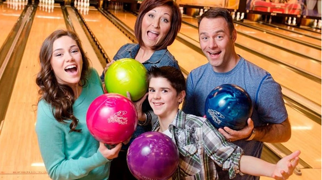 An entire Family of Four Holding Bowling Ball in front of the Bowling Alley